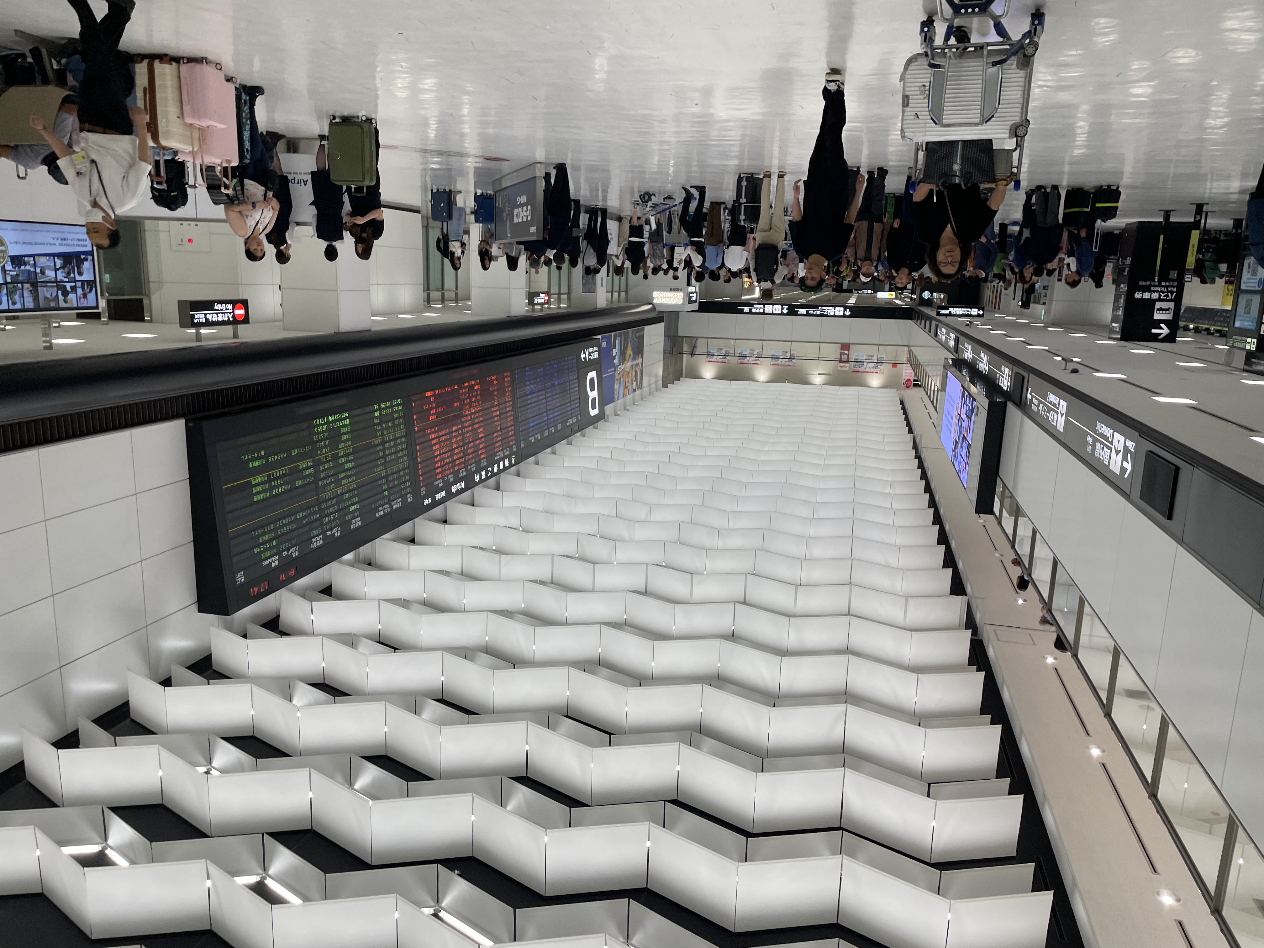 Travellers with luggage in Narita Airport Terminal 2's arrivals hall, beneath the flight information board.